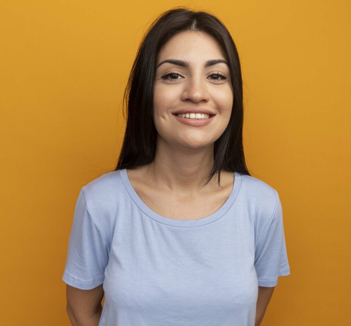 smiling pretty brunette caucasian girl looks at camera isolated on orange background with copy space